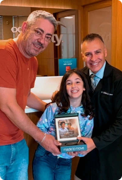 Dr. Claudinei dos Santos com paciente infantil e responsável durante entrega do kit Invisalign na Clínica OdontoQuality.